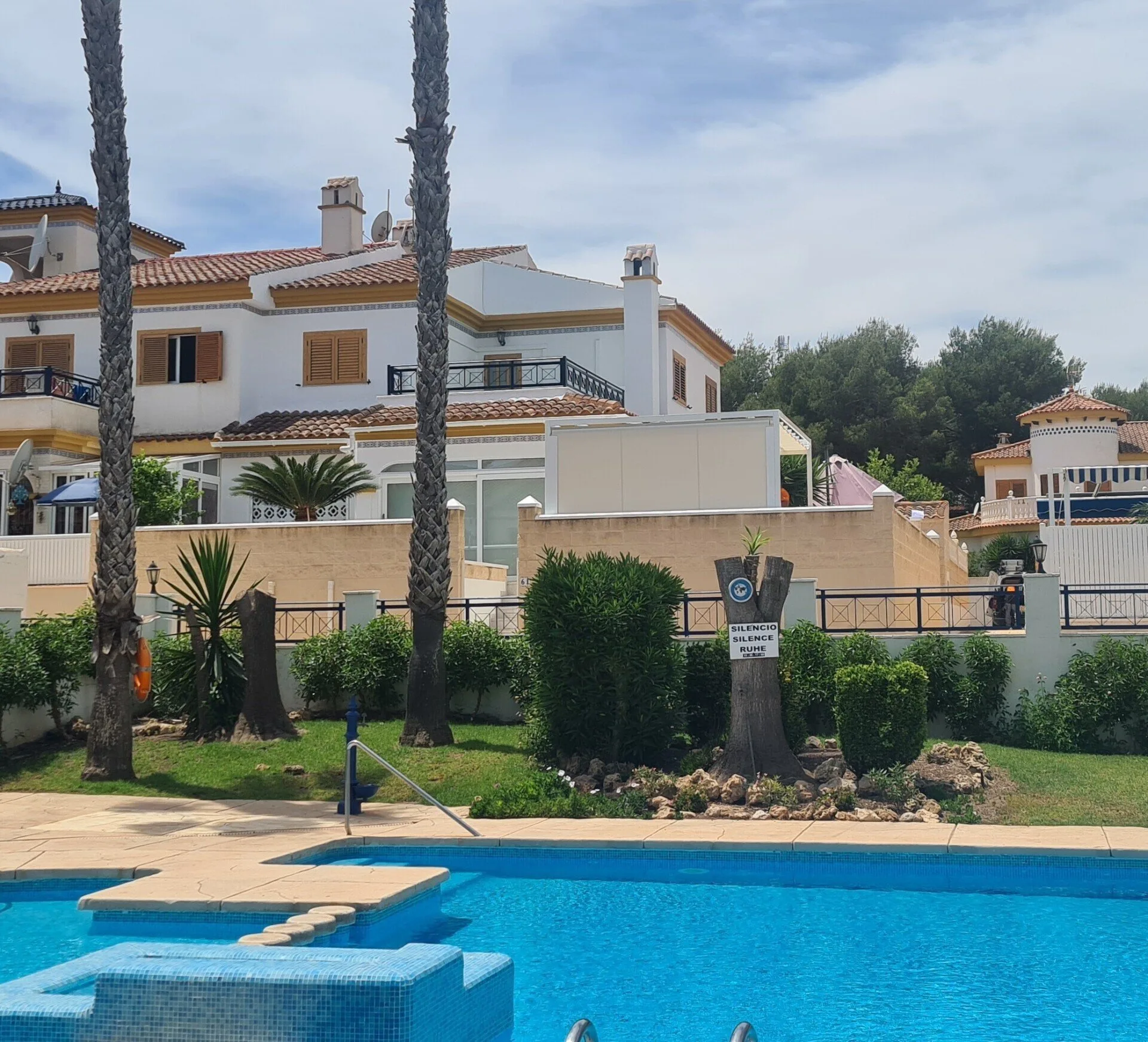 Poolanlage mit Palmen und weißen Häusern unter blauem Himmel